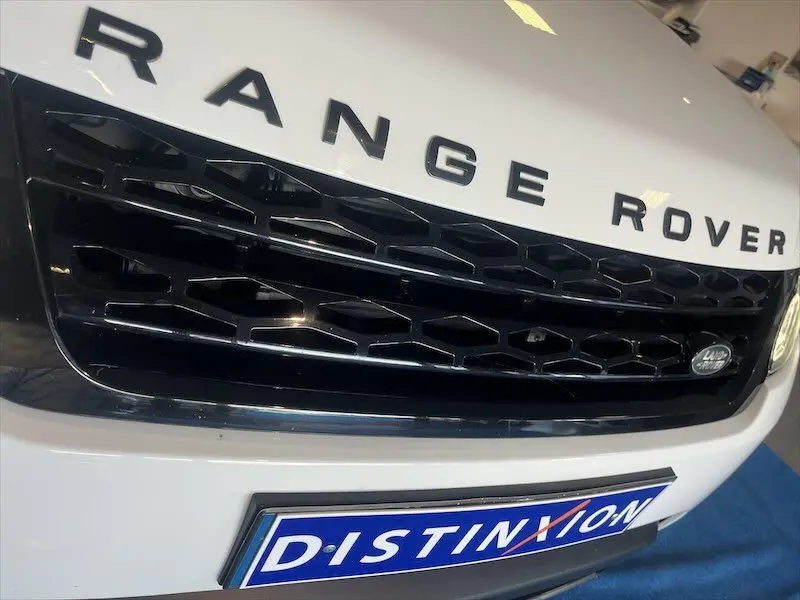Gros plan sur la calandre noire et le capot blanc d'un Range Rover Sport 2018 avec logo Land Rover visible.