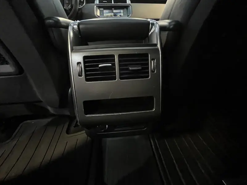Vue rapprochée de la console arrière noire du Range Rover Sport blanc, avec bouches d’aération et prise 12V visibles.