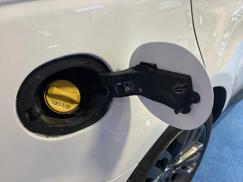 Bouchon de réservoir diesel ouvert sur le côté gauche d'un Range Rover Sport blanc, avec une jante visible en arrière-plan.