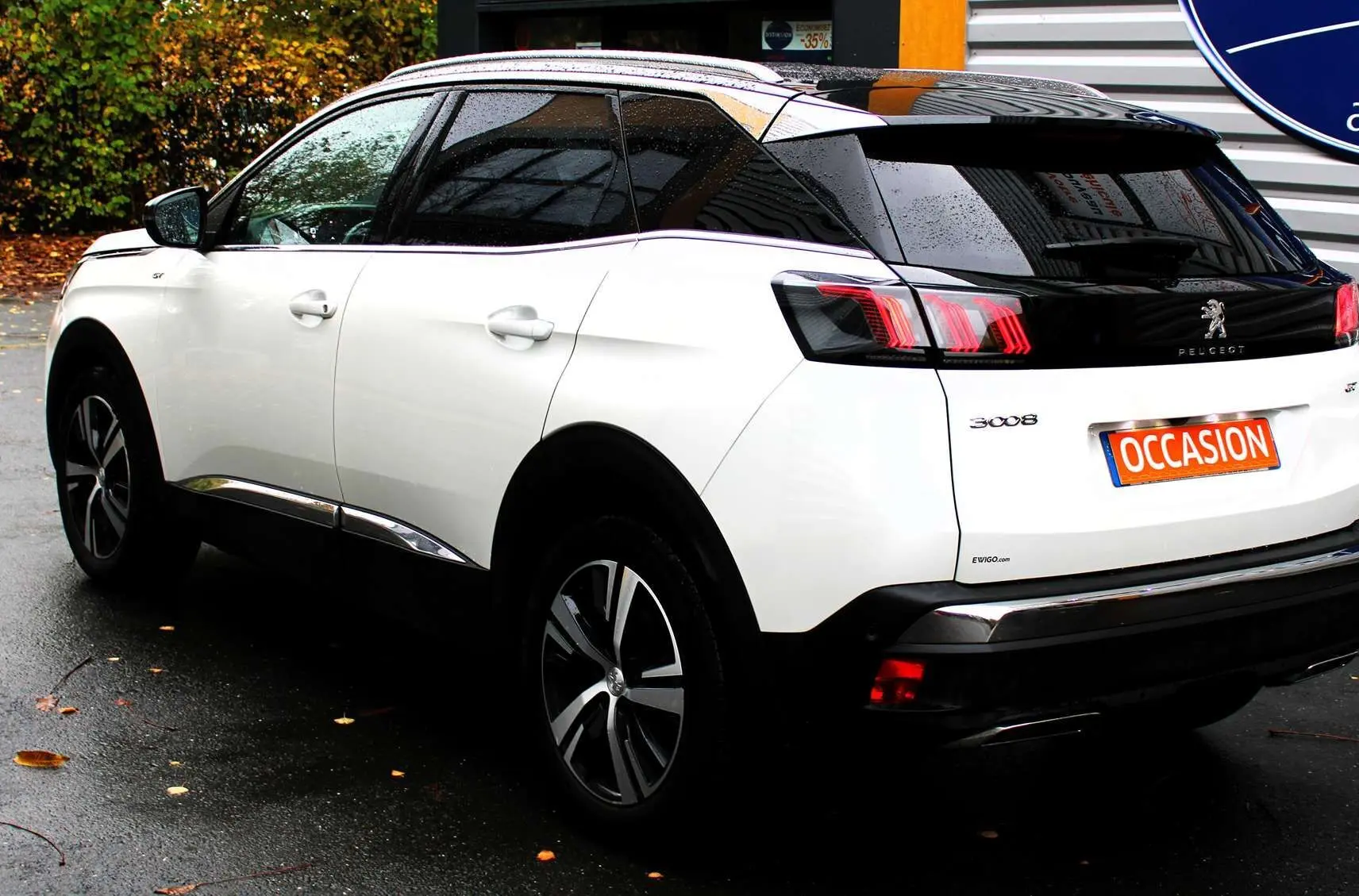 Peugeot 3008 blanc nacré vu de trois quarts arrière droit, toit panoramique noir et feux arrière LED allumés.