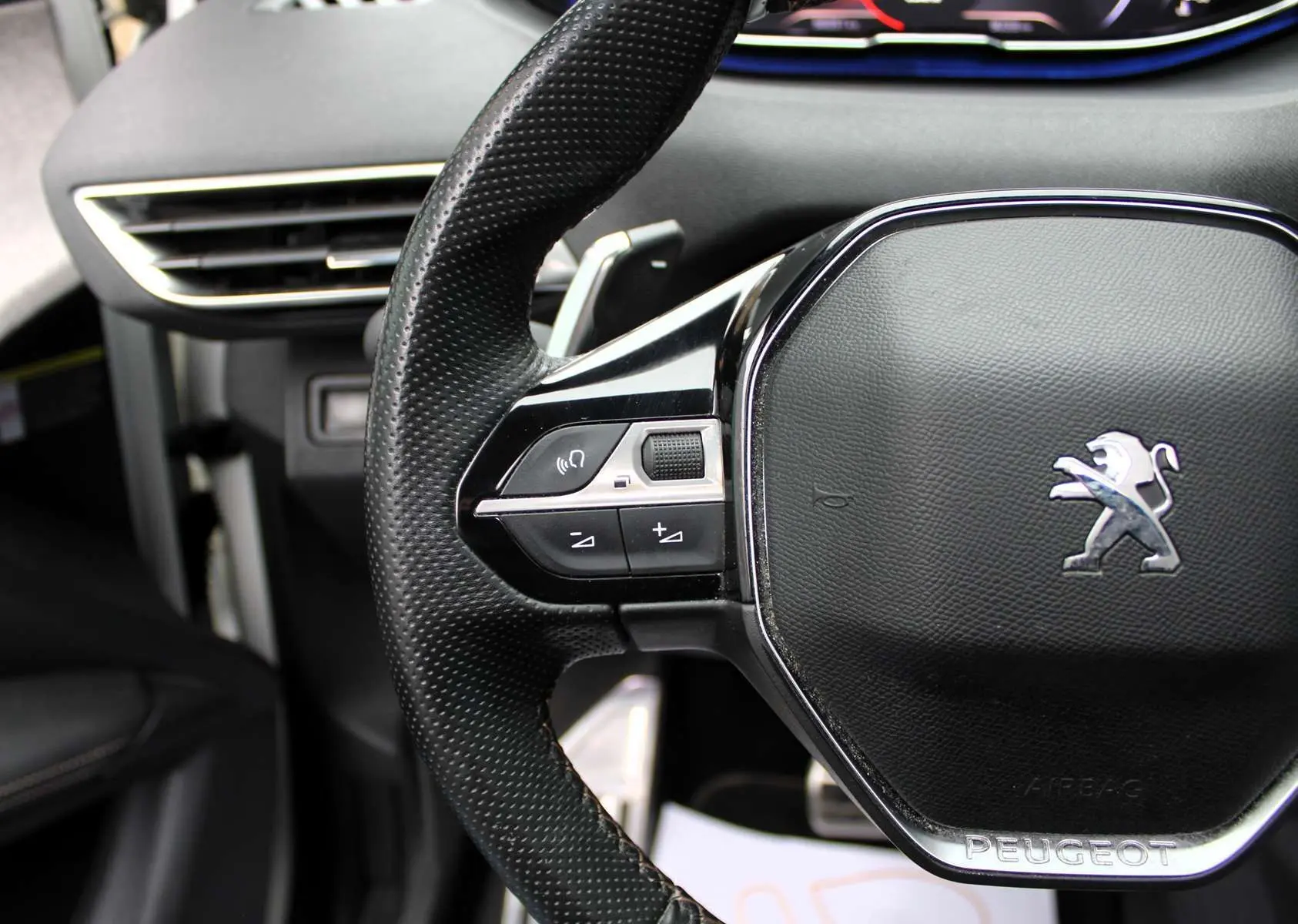 Gros plan sur le volant noir perforé du Peugeot 3008 2025 avec commandes intégrées et logo lion chromé.