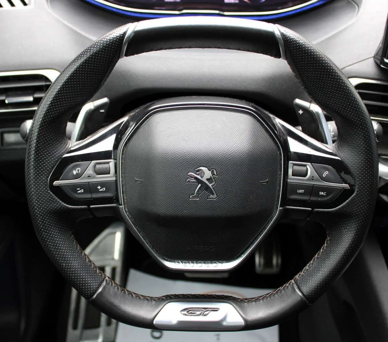 Gros plan sur le volant cuir noir du Peugeot 3008 GT 2025 avec logo lion et badge GT en bas.