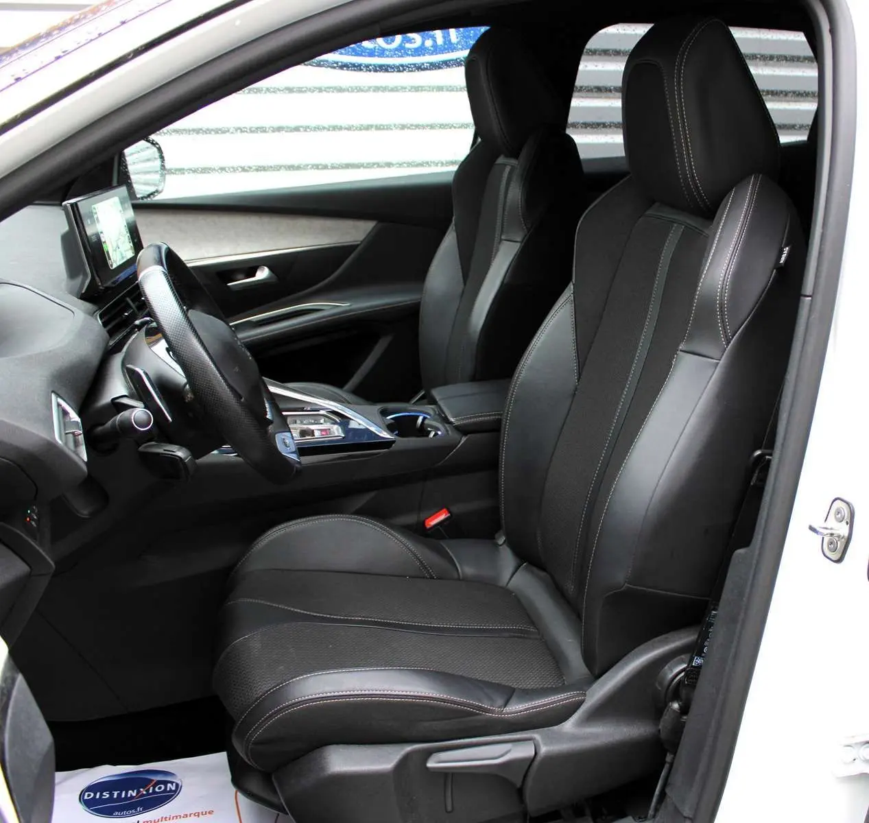 Intérieur côté conducteur du Peugeot 3008 blanc nacré 2025, sièges noirs en cuir avec surpiqûres contrastées et tableau de bord moderne.