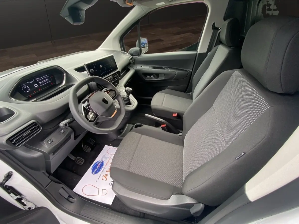 Vue intérieure côté conducteur du Peugeot Partner blanc 2024, montrant le tableau de bord numérique et les sièges gris.