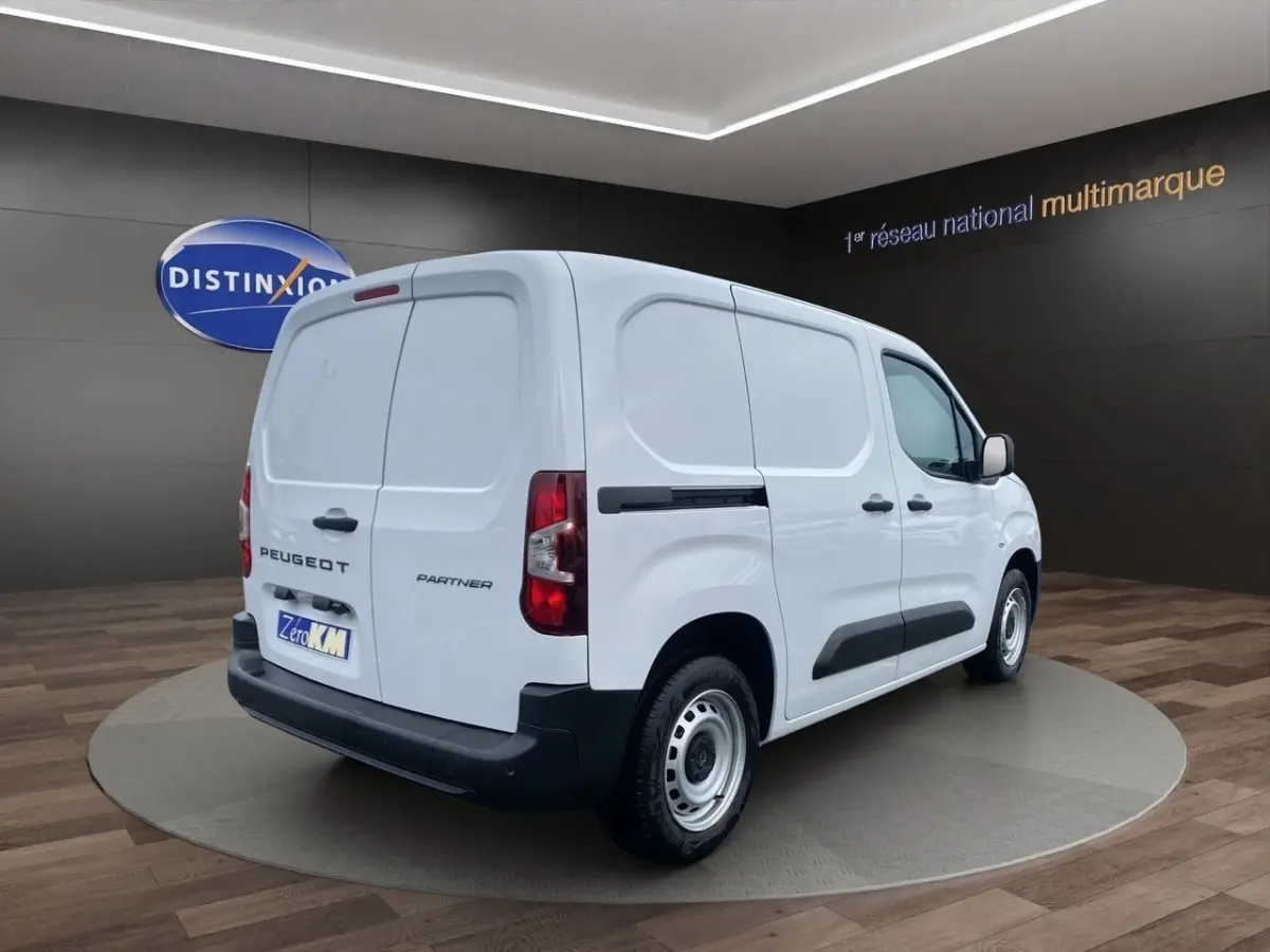 Vue 3/4 arrière droite du Peugeot Partner blanc utilitaire avec portes arrière battantes et protections noires latérales.