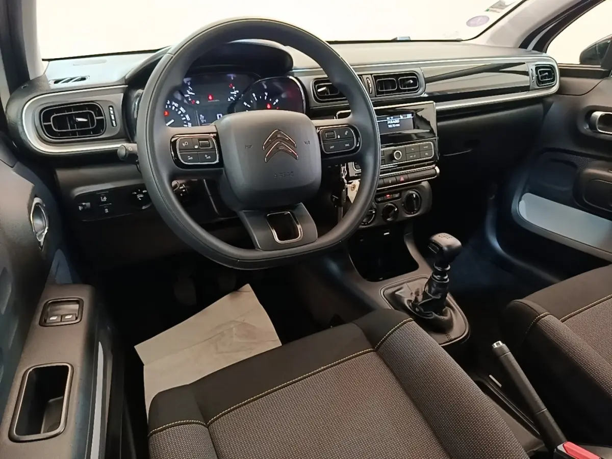 Vue intérieure avant centrée sur le volant multifonctions et la console centrale d'une Citroën C3 blanche de 2019 avec boîte manuelle.