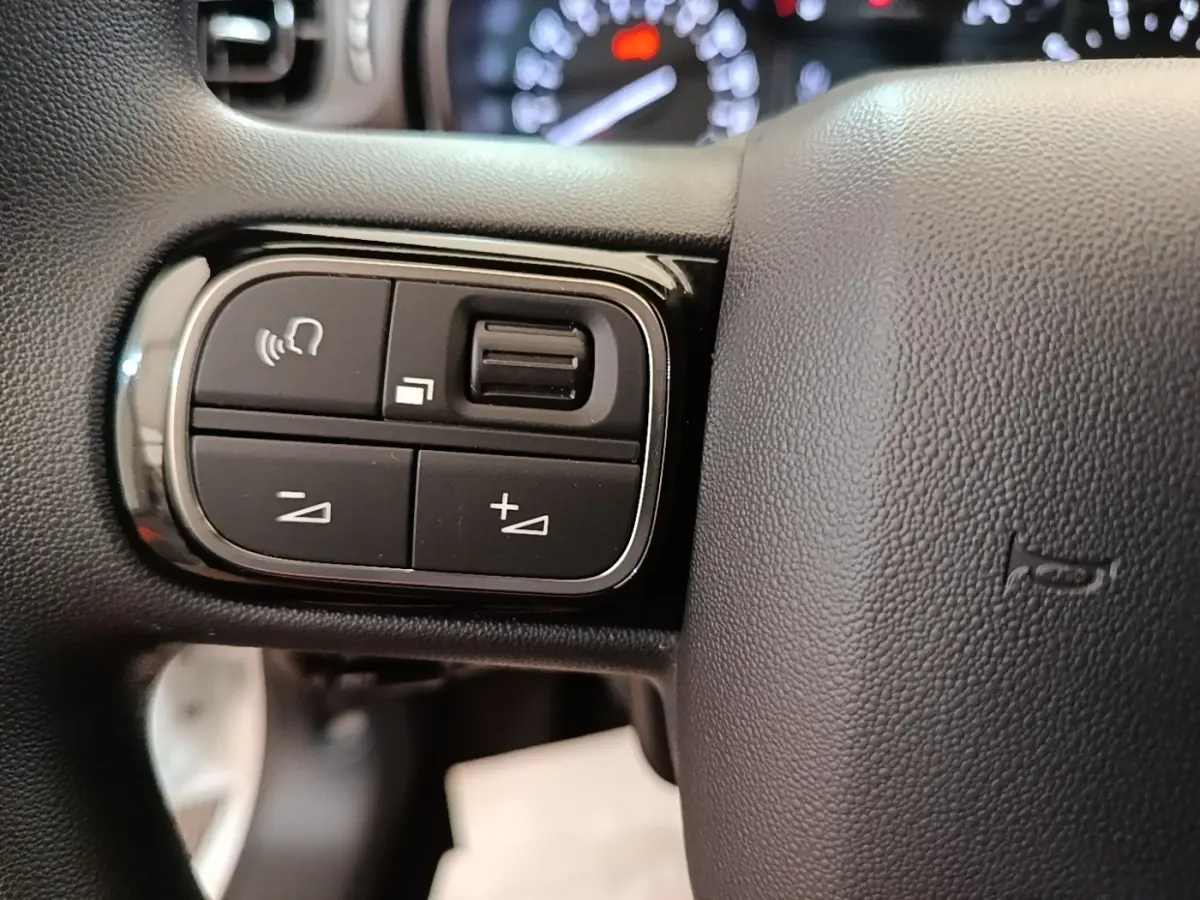 Gros plan sur les commandes gauche du volant noir d'une Citroën C3 blanche, avec boutons de volume et appel mains libres.