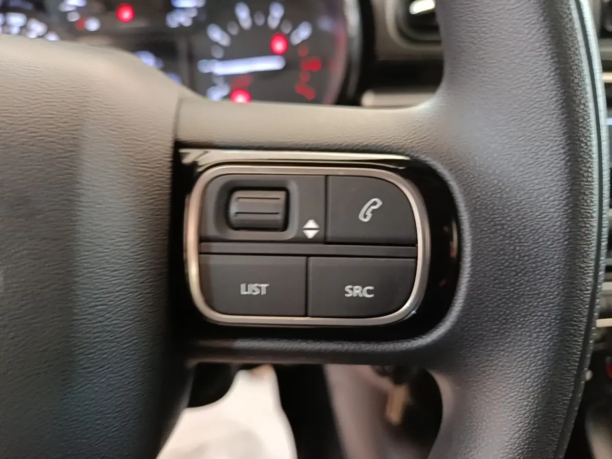 Gros plan sur les commandes multifonctions noires du volant de la Citroën C3 PureTech 110 blanc, avec tableau de bord flou en arrière-plan.