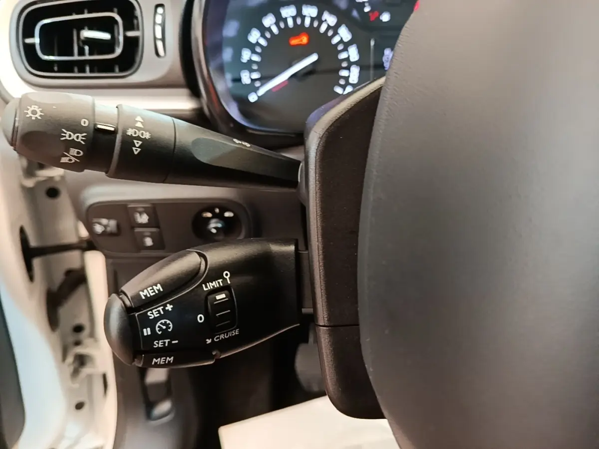 Gros plan sur la colonne de direction et commandes du régulateur de vitesse d'une Citroën C3 blanche, intérieur clair.