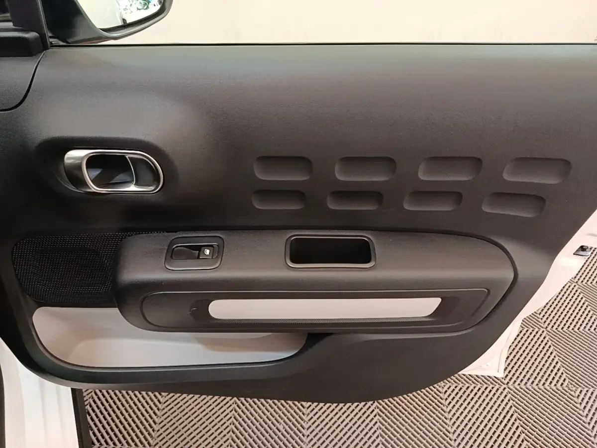 Vue rapprochée de la porte intérieure côté gauche d'une Citroën C3 blanche, avec poignée et commande de vitre.