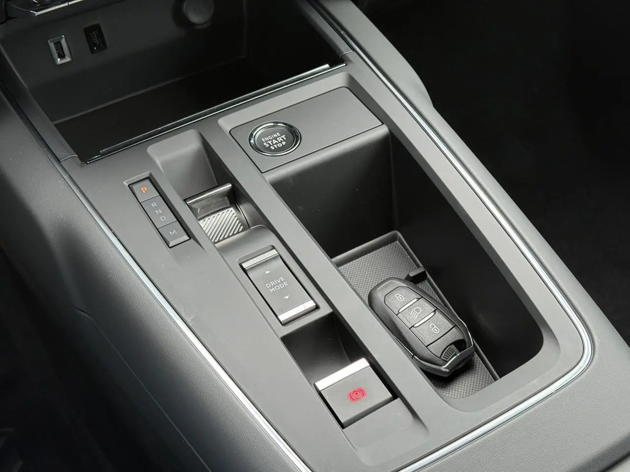 Gros plan sur la console centrale noire du Citroën C5 Aircross Hybrid 2025 avec bouton start/stop et clé mains-libres.