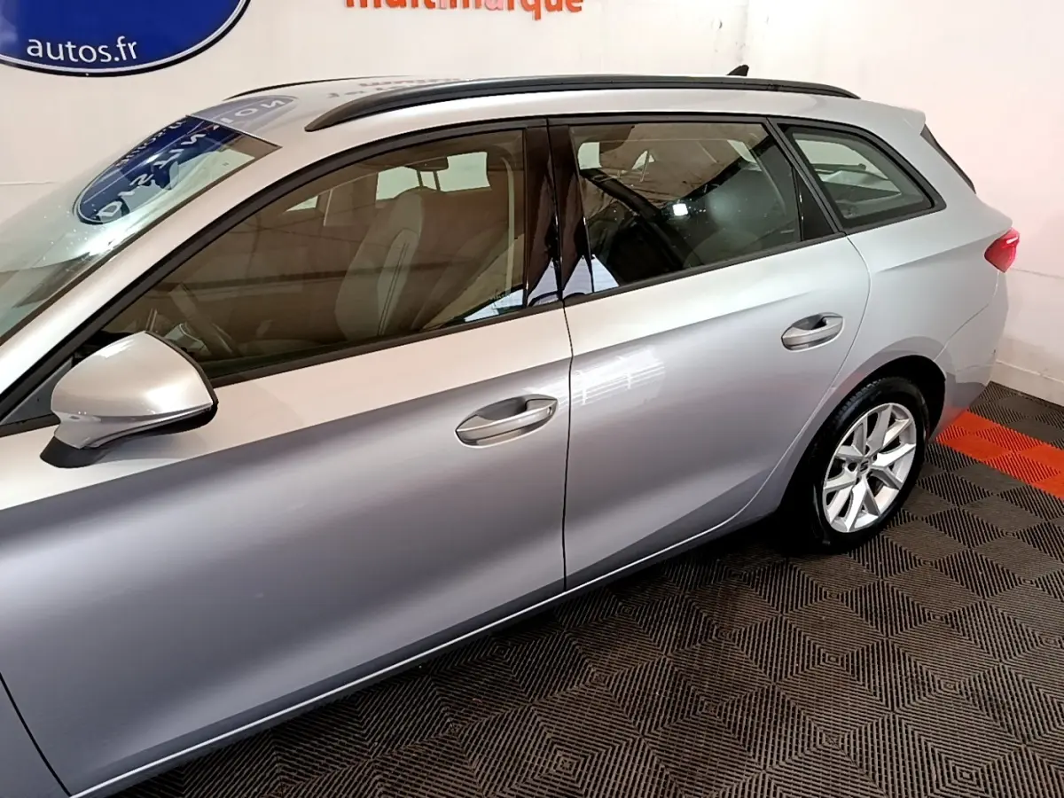 Vue latérale gauche d'une SEAT Leon gris clair en intérieur, mettant en valeur ses lignes fluides et ses jantes alliage.