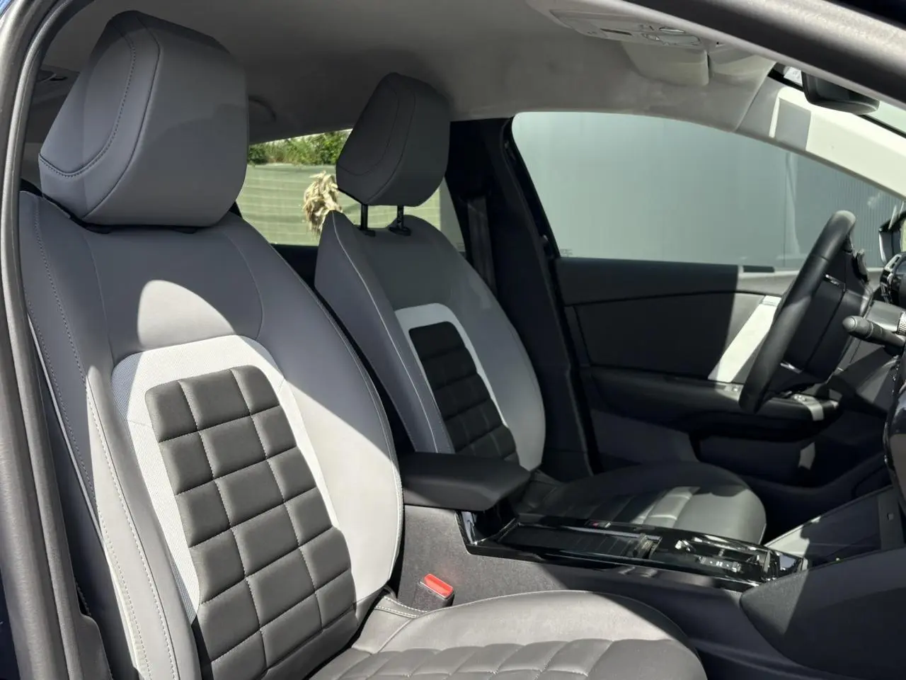 Vue intérieure côté gauche des sièges avant gris clair et noir avec accoudoir central et volant de la Citroën C4 Hybrid 2025.