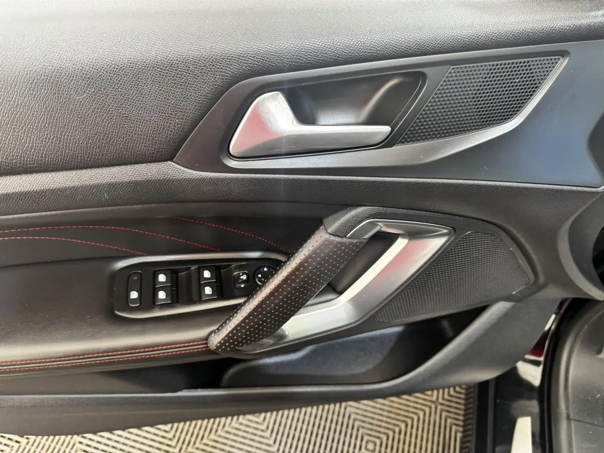 Gros plan sur la porte intérieure côté conducteur noire avec surpiqûres rouges et commandes des vitres du Peugeot 308 GT Line.