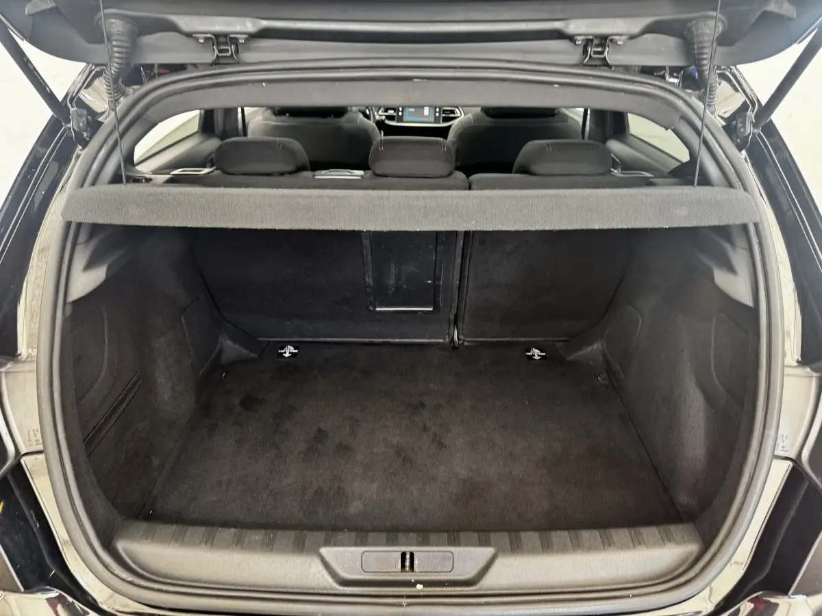 Vue arrière du coffre ouvert d'une Peugeot 308 noire, montrant l'espace de chargement et la banquette arrière rabattue partiellement.