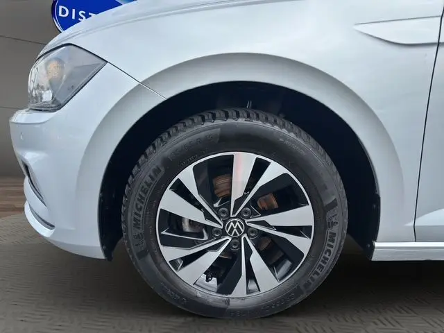 Gros plan sur la roue avant gauche d'une Volkswagen Polo gris clair, avec partie avant et phare visibles.