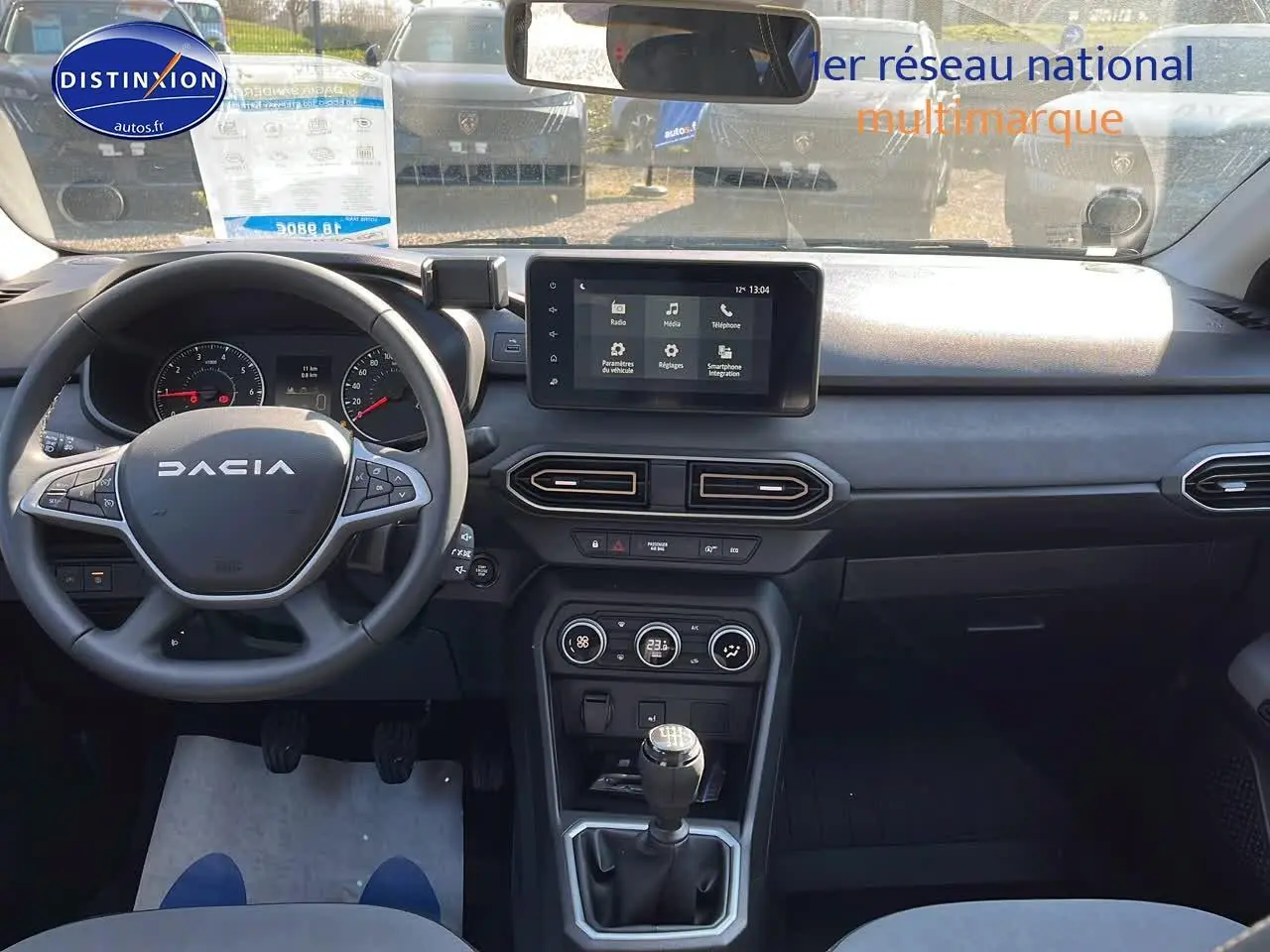 Vue intérieure avant du tableau de bord et volant DACIA Sandero 2025 avec écran tactile et levier de vitesses manuel.