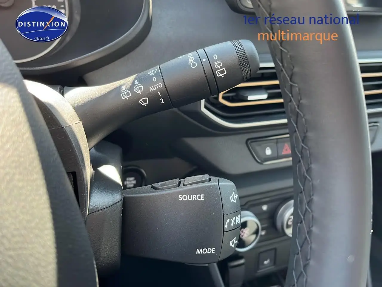 Gros plan sur les commandes au volant et manette d'essuie-glace d'une Dacia Sandero 2025 vert cèdre, intérieur noir.