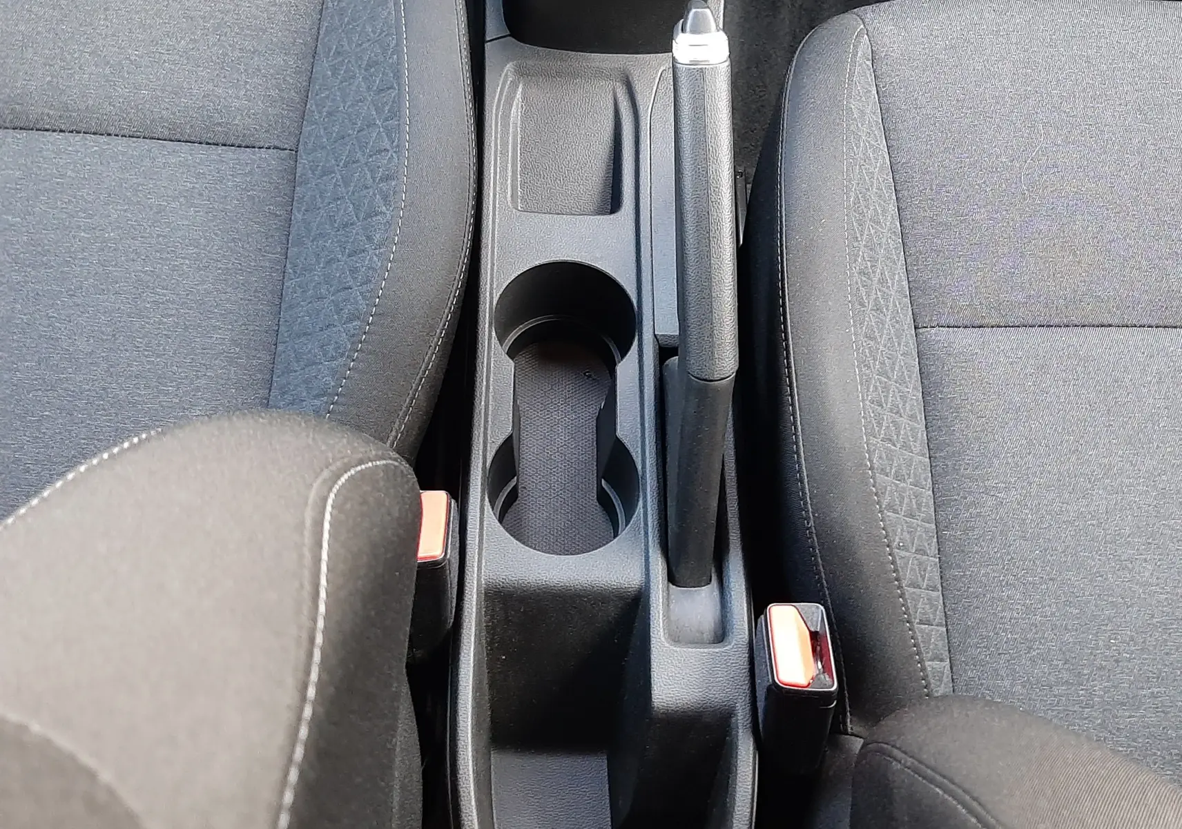 Vue plongeante sur la console centrale noire de la Renault Clio V avec frein à main manuel et sièges tissu noir.