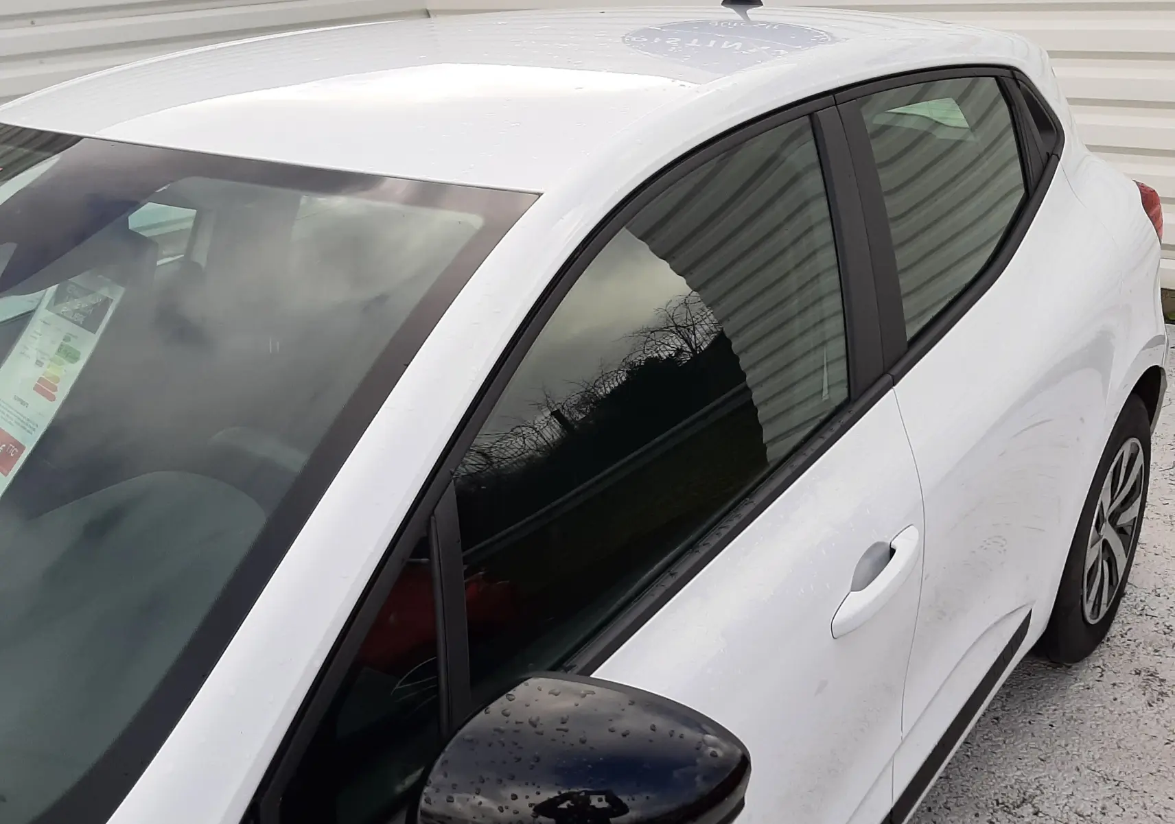 Vue 3/4 avant droit d'une Renault Clio V blanche avec rétroviseur noir et vitres teintées.