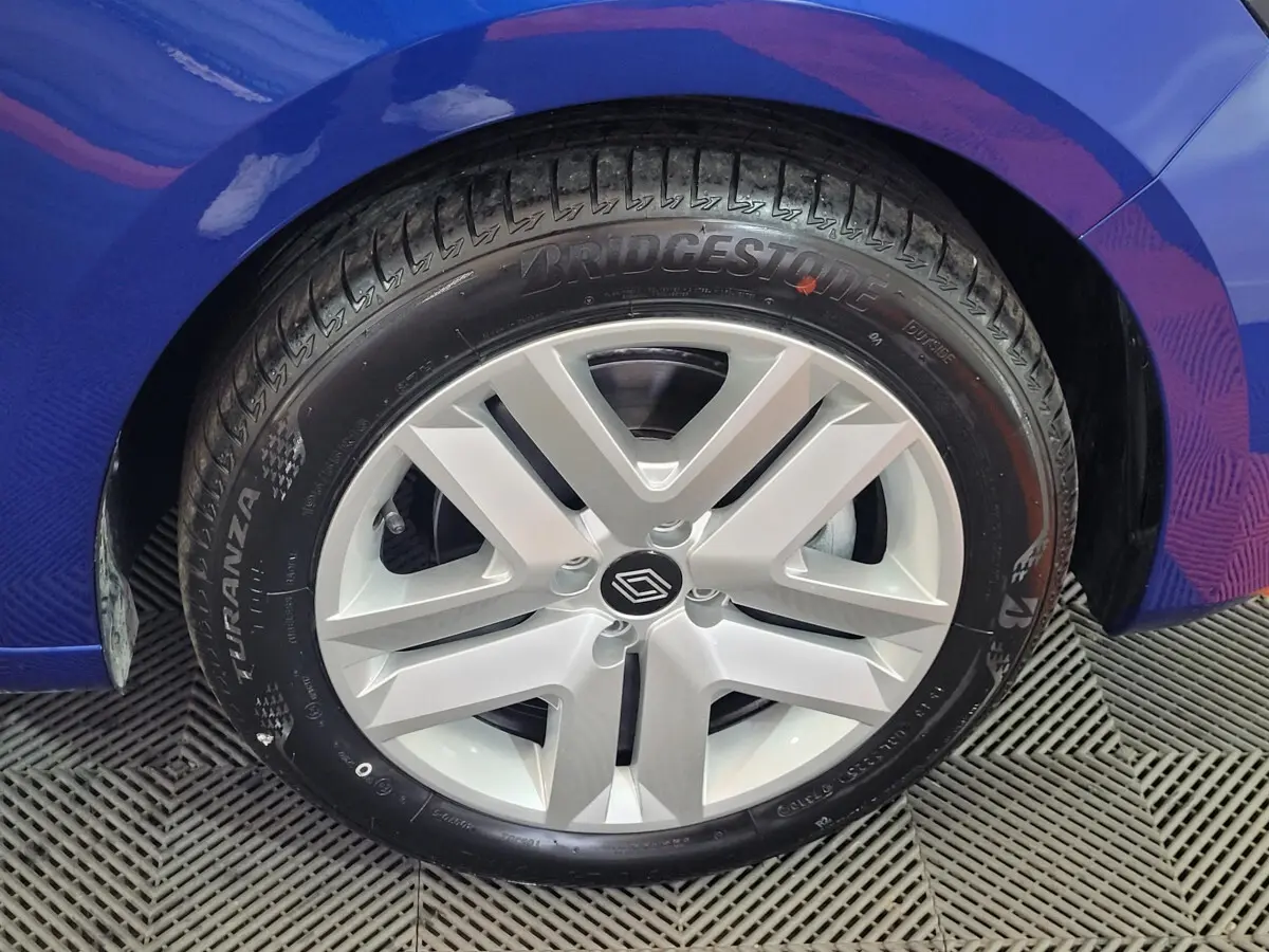 Gros plan sur la roue avant droite d’une Renault Clio bleu, avec jante argentée au design moderne.