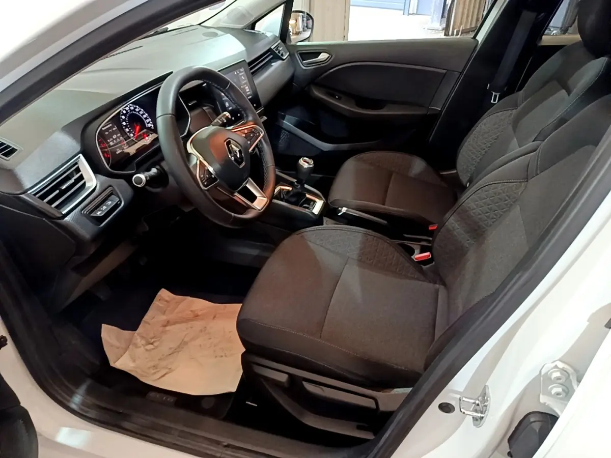 Vue intérieure côté conducteur de la Renault Clio Business blanche, montrant le volant cuir et la console avec boîte manuelle.