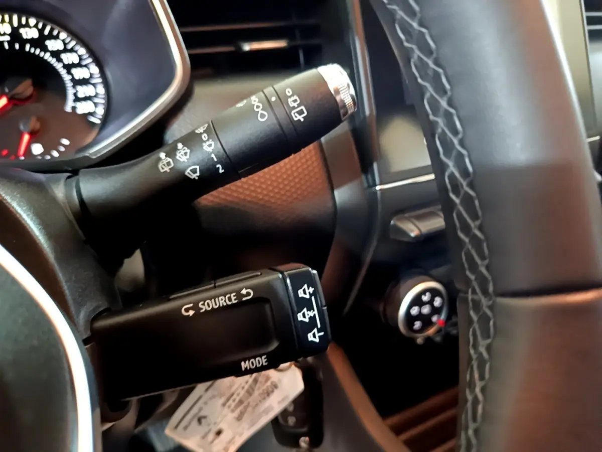 Gros plan sur les commandes au volant côté gauche d’une Renault Clio Business blanche, avec tableau de bord partiellement visible.