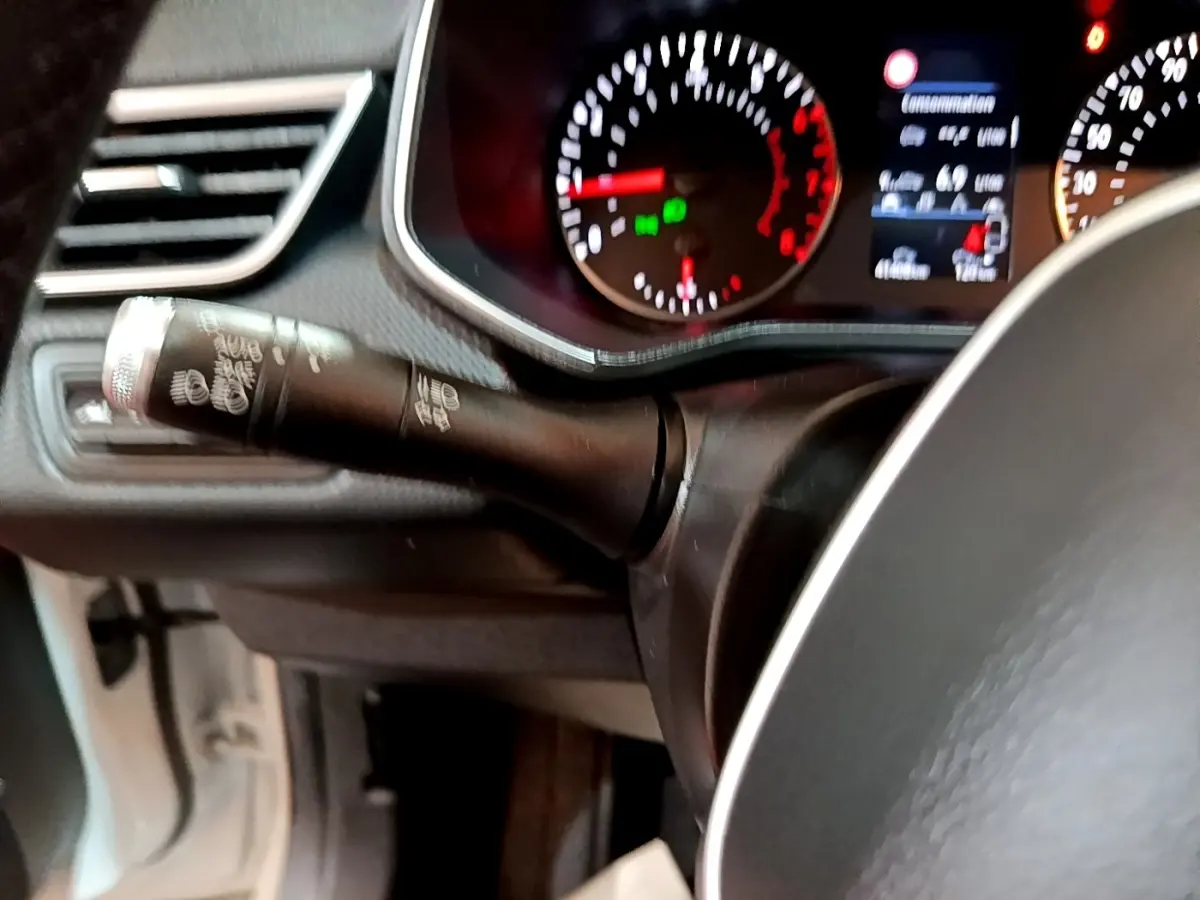 Gros plan sur le commodo de clignotant noir et le tableau de bord éclairé de la Renault Clio Business blanche de 2021.