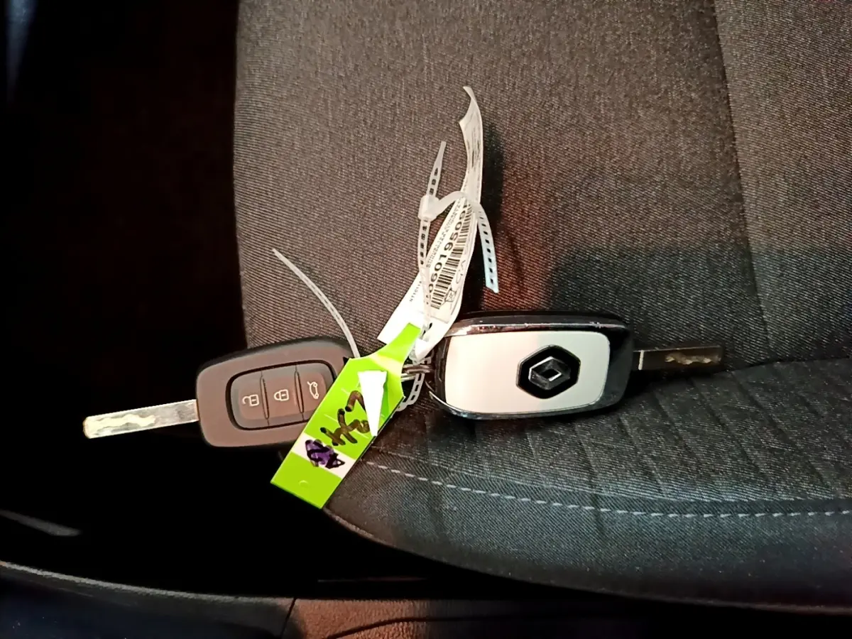Clés de voiture Renault posées sur un siège en tissu gris foncé, sans vue du véhicule.