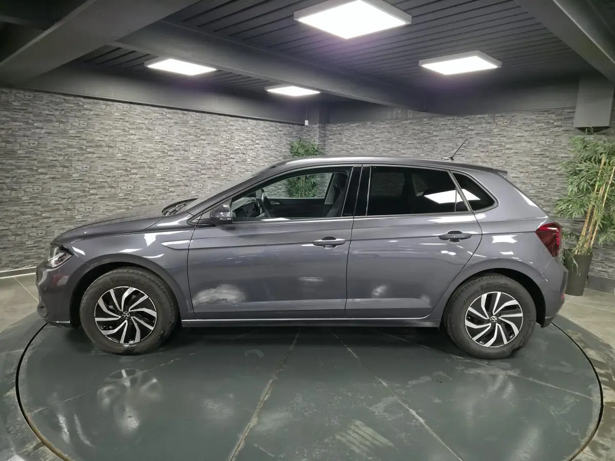 Profil côté gauche d'une Volkswagen Polo gris métallisé 2025 avec jantes alliage et vitres arrière surteintées dans un showroom.