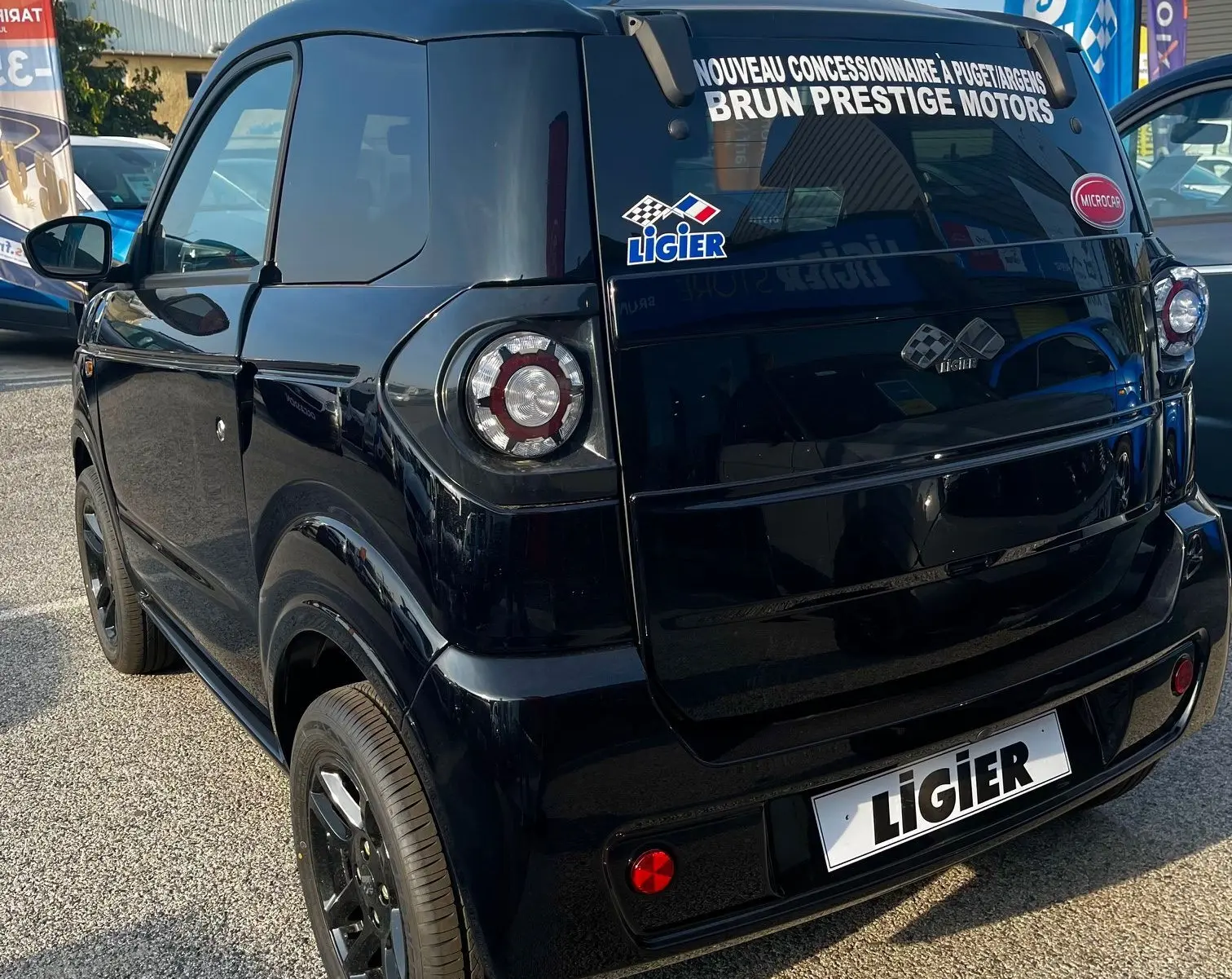 Vue 3/4 arrière droite d'une Ligier Myli électrique noire intense 2024 avec stickers concessionnaire sur la lunette arrière.