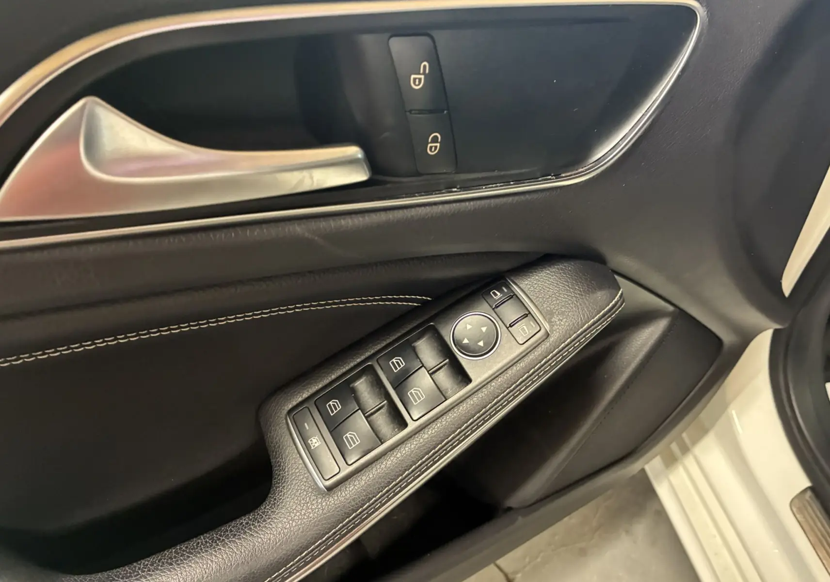 Gros plan sur la porte côté conducteur d'une Mercedes Classe A blanche, montrant les commandes de vitres et la poignée intérieure argentée.