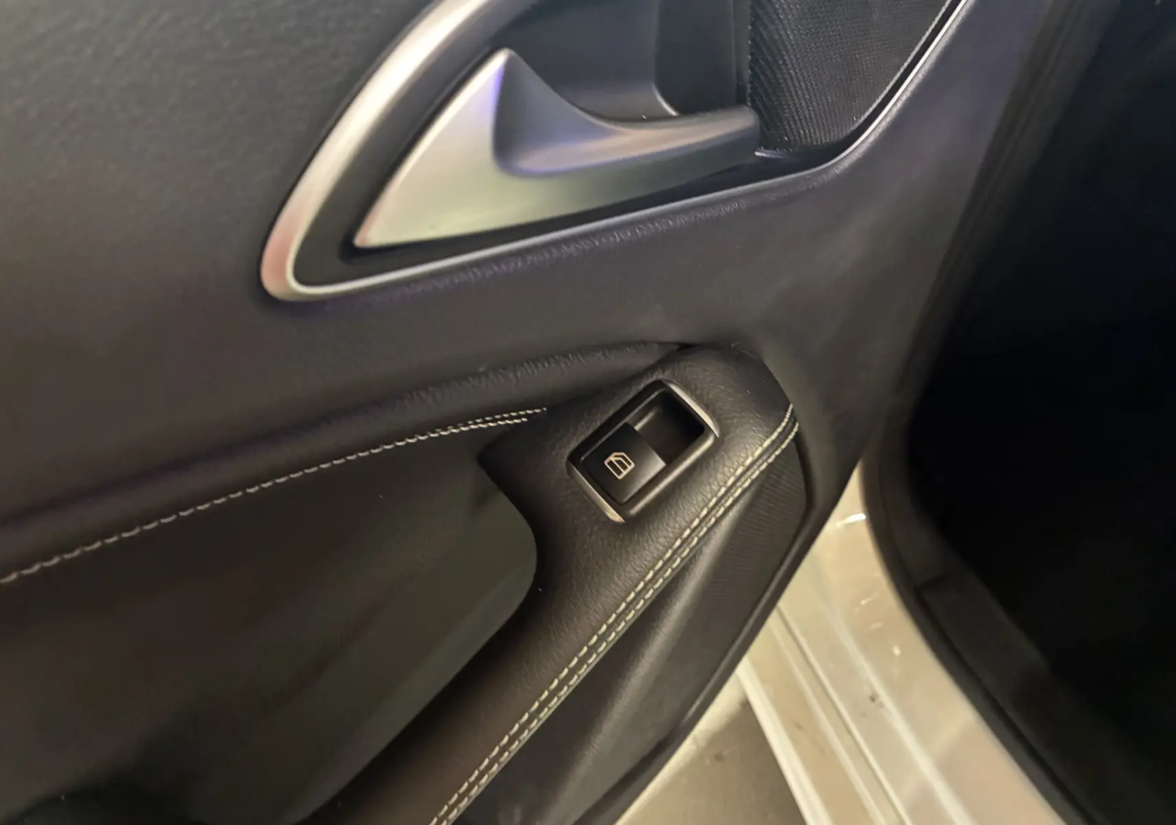 Gros plan sur la poignée intérieure et le bouton de lève-vitre côté conducteur d'une Mercedes Classe A blanche de 2016.