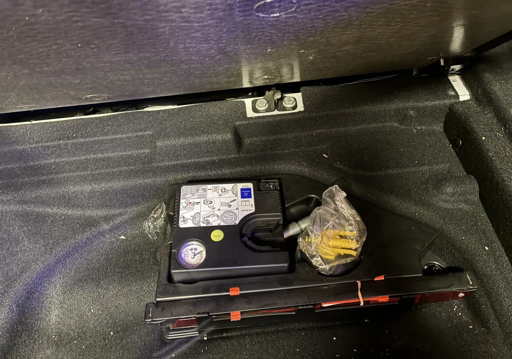 Gros plan sur le compresseur et kit de réparation de pneu dans le coffre d'une Mercedes Classe A blanche 2016.