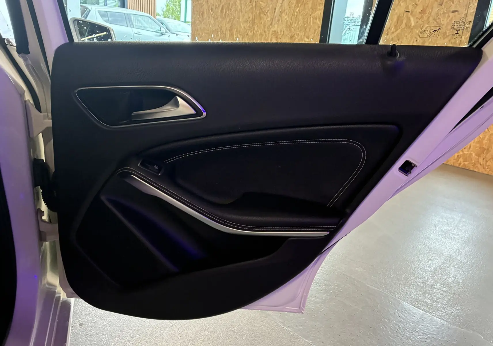 Vue intérieure de la porte arrière gauche d'une Mercedes Classe A 200D blanche, garniture cuir noir avec surpiqûres blanches.