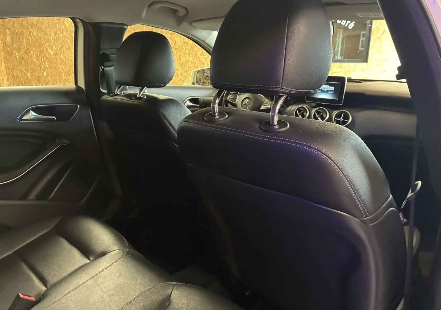 Intérieur noir cuir d'une Mercedes Classe A 200D 2016 vu depuis l'arrière côté gauche, avec tableau de bord et écran visible.