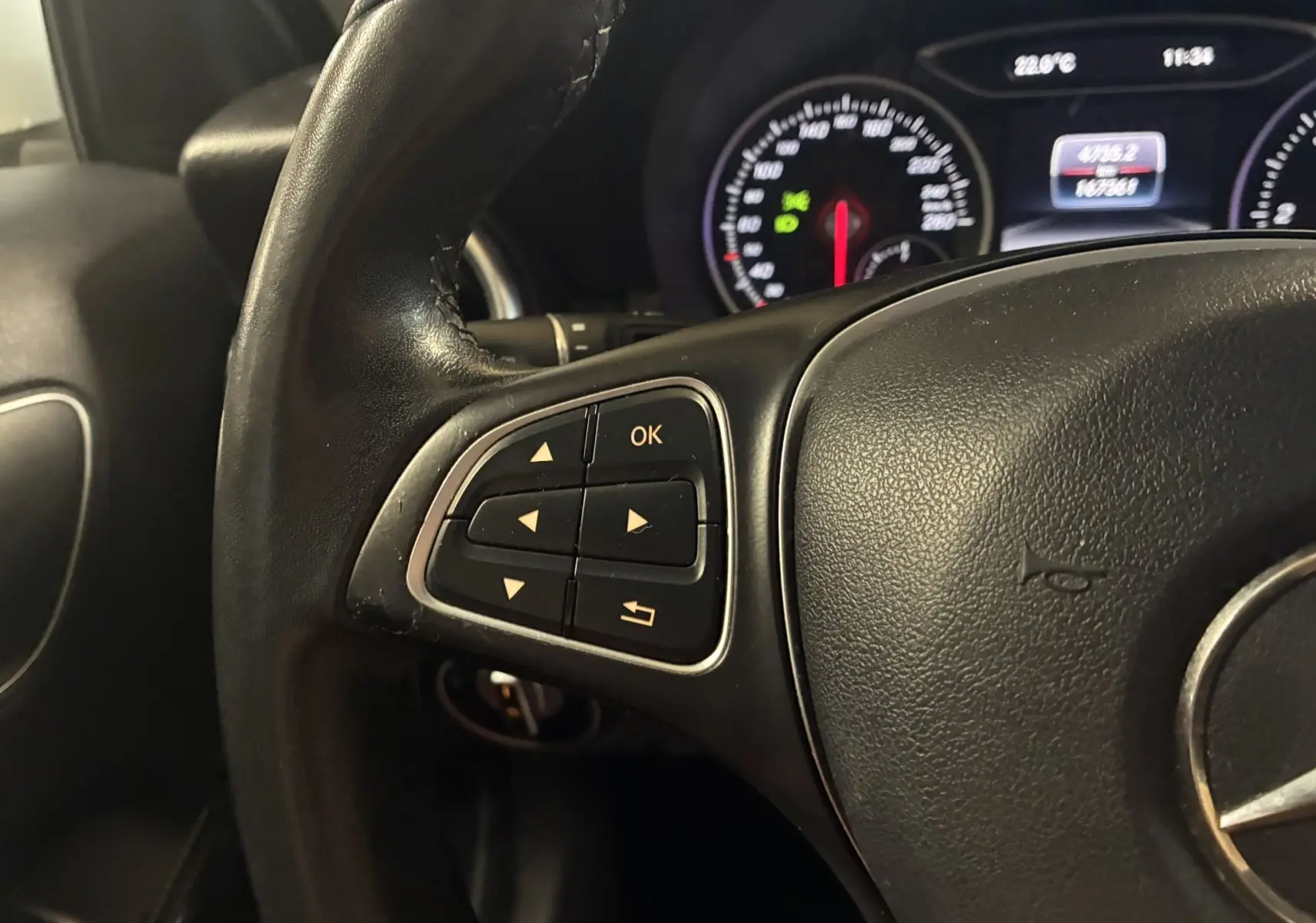 Gros plan sur le volant cuir noir de la Mercedes Classe A 200D 2016, avec commandes multifonctions et tableau de bord éclairé.