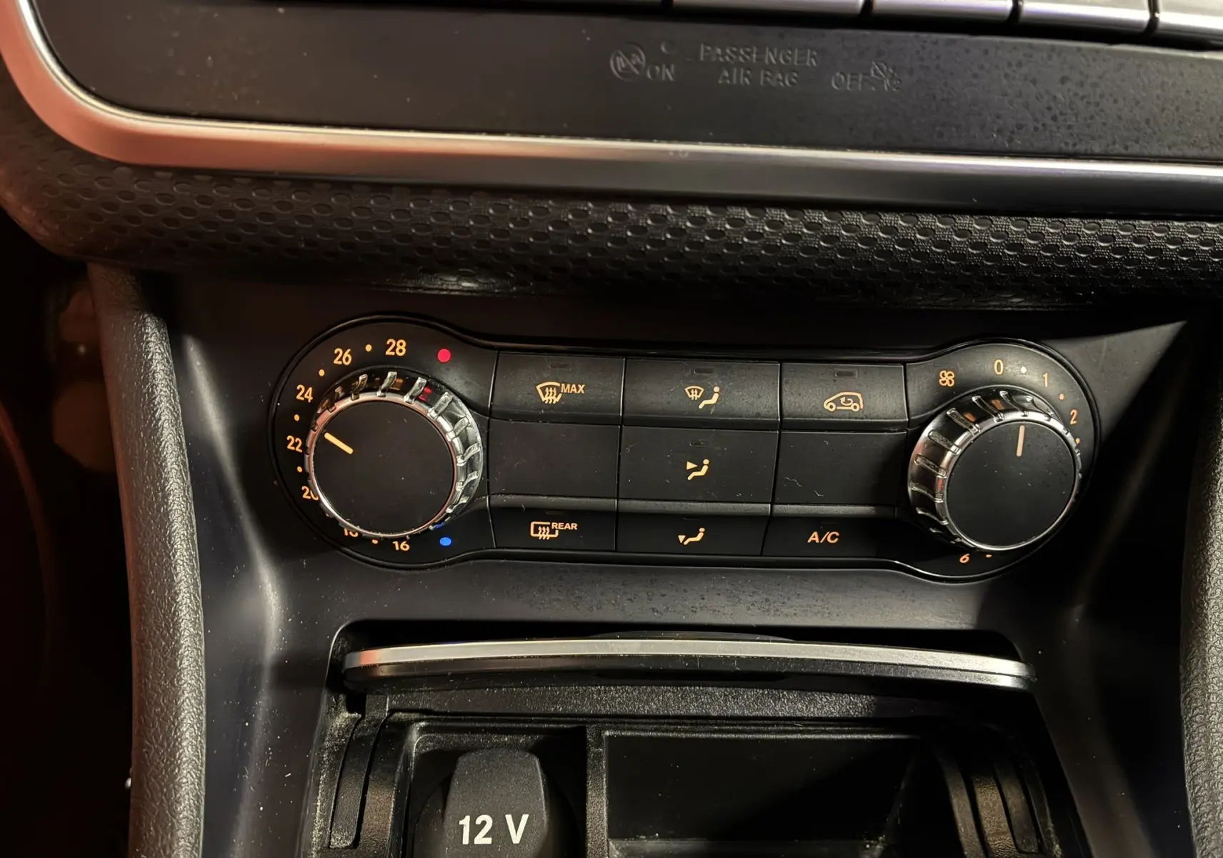 Gros plan sur la commande de climatisation et prise 12V du tableau de bord d'une Mercedes Classe A 200D blanche de 2016.