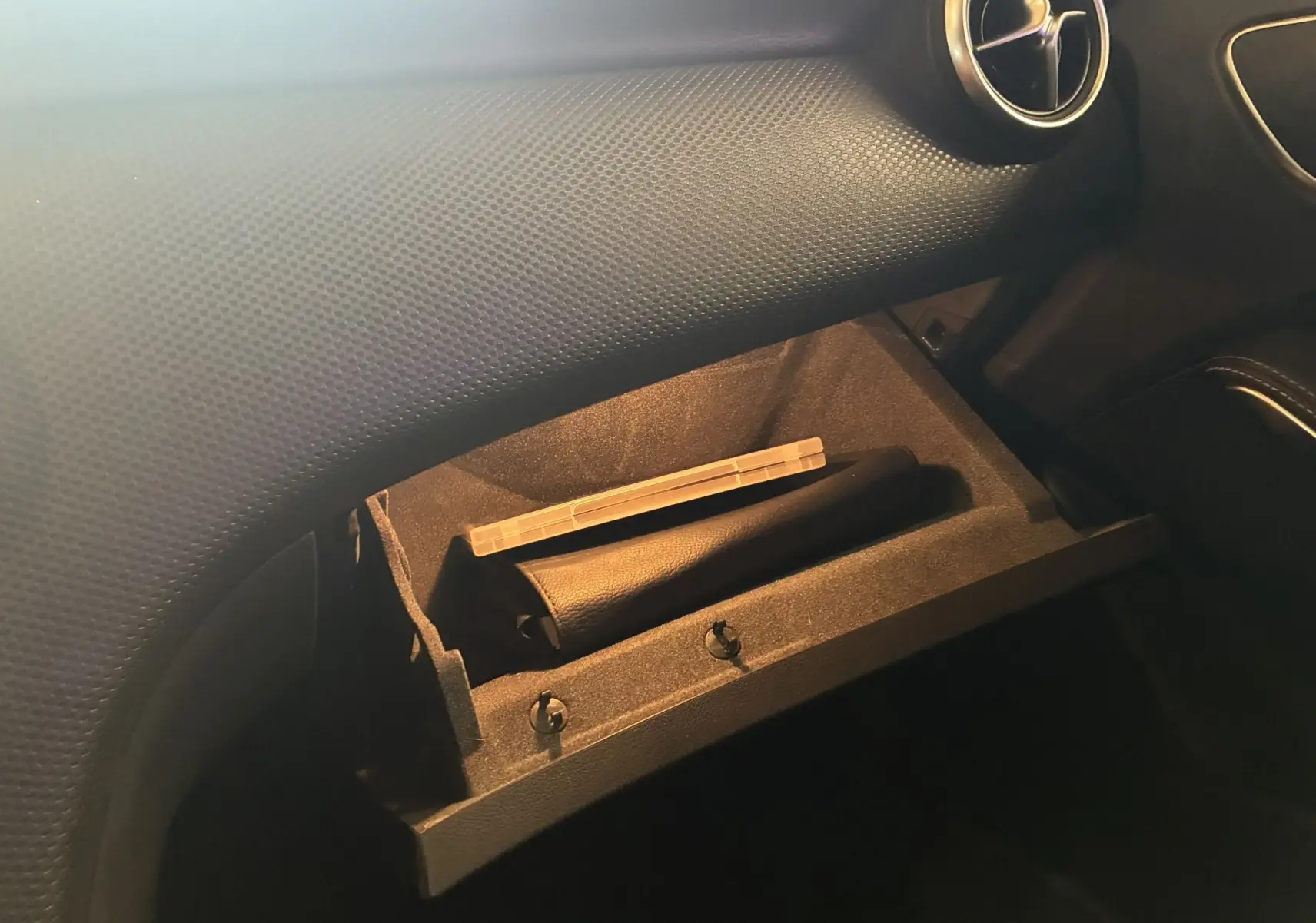 Gros plan sur la boîte à gants ouverte du Mercedes Classe A 200D 2016, intérieur noir avec détails en cuir et aérateur rond.