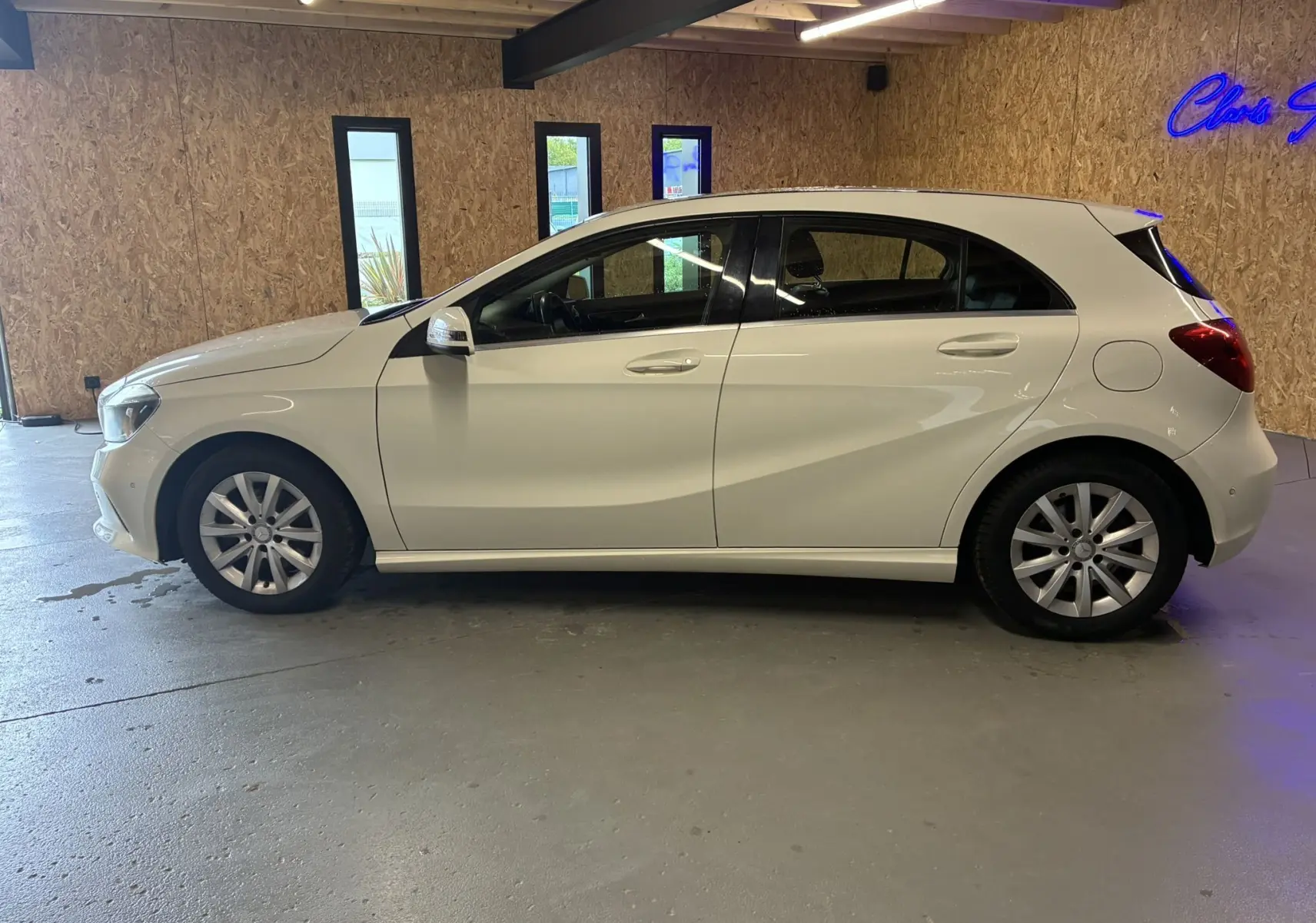 Profil côté gauche d'une Mercedes Classe A 200D blanche de 2016, compacte avec cinq portes, dans un garage éclairé.