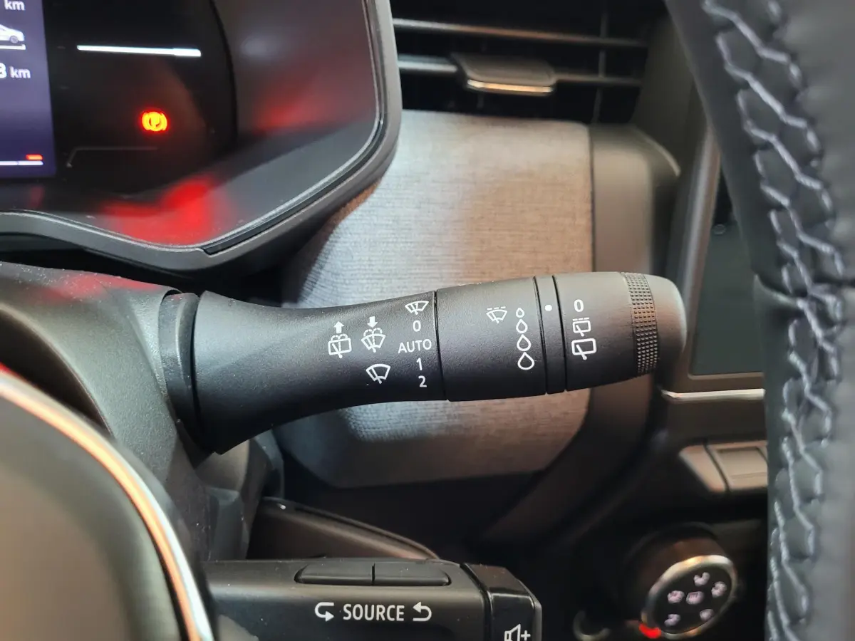 Gros plan sur la commande des essuie-glaces à gauche du volant dans l'habitacle gris d'une Renault Clio bleu.