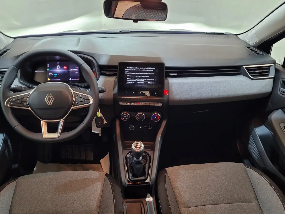 Vue intérieure avant de la Renault Clio Evolution Blue dCi 100 2025, tableau de bord gris et volant cuir noir avec écran tactile central.