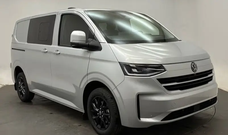 Vue 3/4 avant droite d’un Volkswagen Transporter T7 ProCab Business 2026 en gris graphite avec jantes noires, stationné en extérieur.