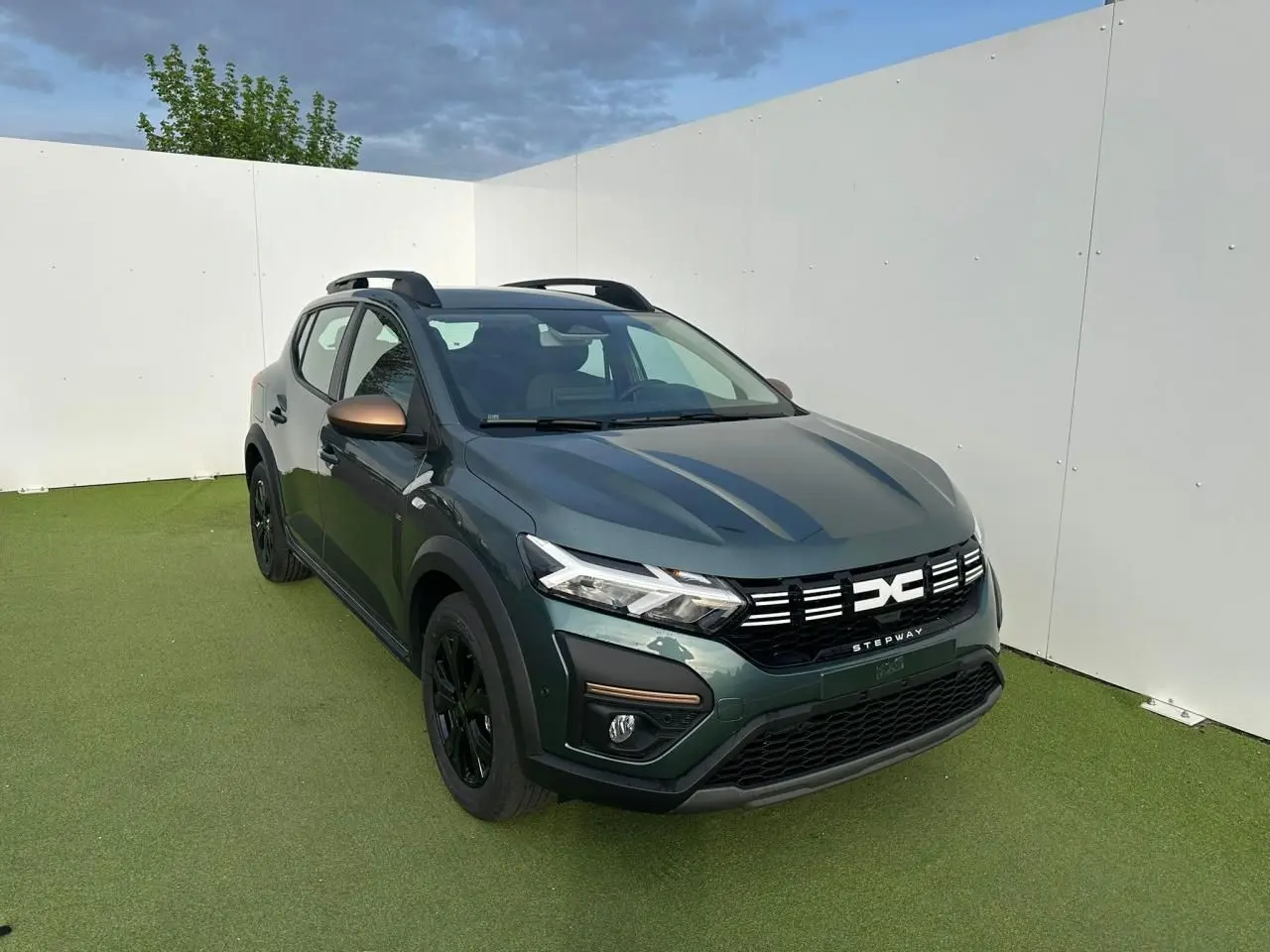 Dacia Sandero III Stepway vert cèdre en 3/4 avant droit avec détails brun cuivré et jantes noires.