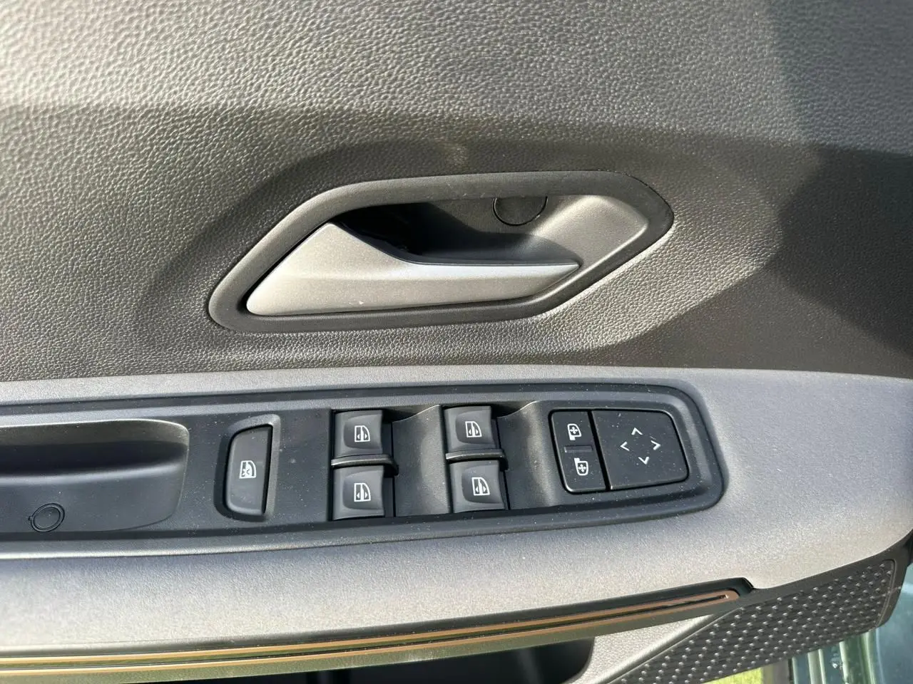 Gros plan sur la commande des vitres électriques et poignée intérieure côté conducteur de la Dacia Sandero III Stepway vert cèdre.
