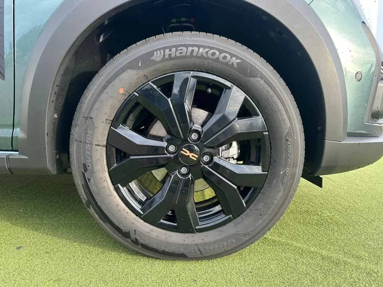 Gros plan sur la roue avant gauche noire brillante d'une Dacia Sandero III Stepway vert cèdre avec jante aluminium 16 pouces.