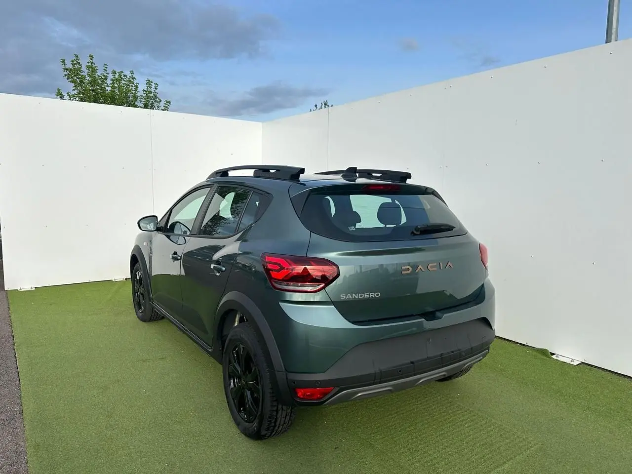 Vue 3/4 arrière droite d'une Dacia Sandero III Stepway vert cèdre avec barres de toit et jantes noires.