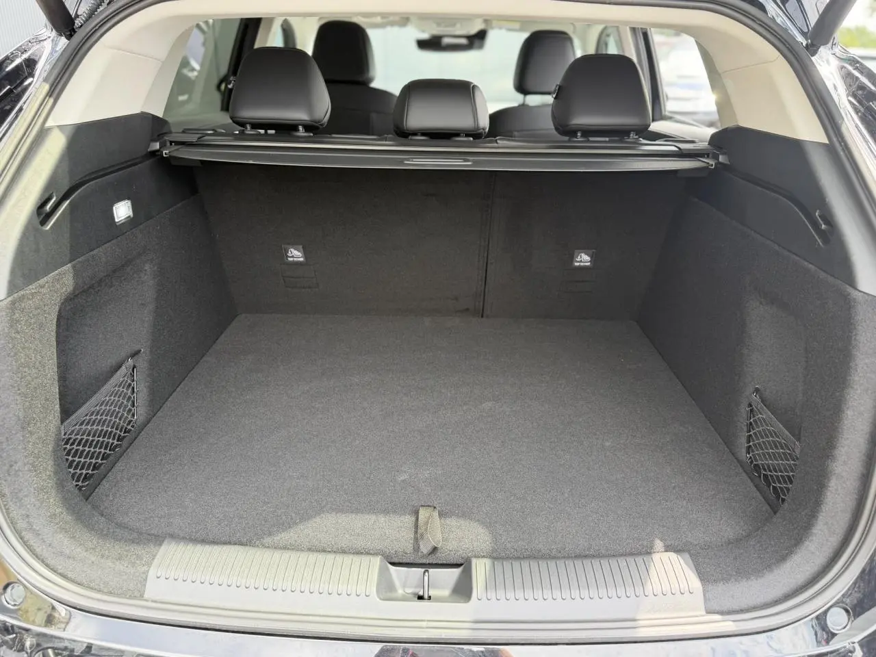 Coffre ouvert vu de l'arrière d'un MG Motor EHS noir, intérieur noir avec filet de rangement latéral.