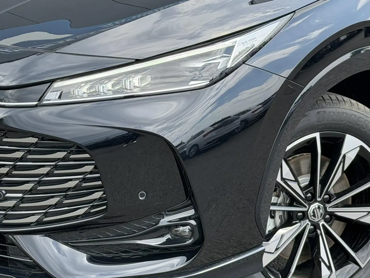 Gros plan sur l'avant droit noir métallisé du MG EHS 1.5 Hybrid+ 224 Luxury avec phares LED et jante alliage 19 pouces.
