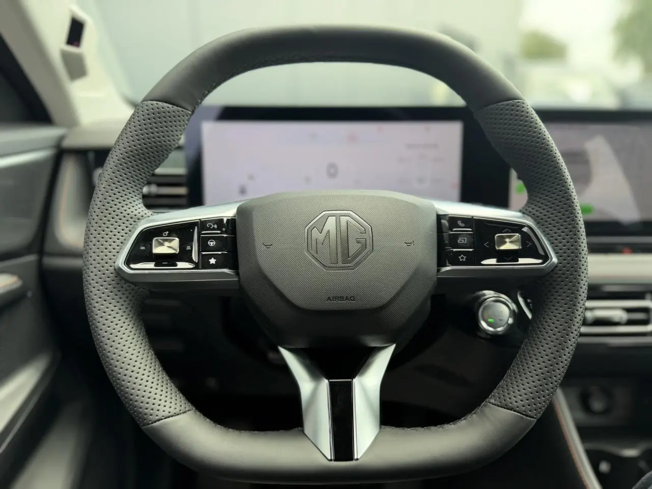 Vue rapprochée du volant noir perforé de la MG MOTOR EHS 1.5 Hybrid+ 224 Luxury avec logo MG central et commandes intégrées.